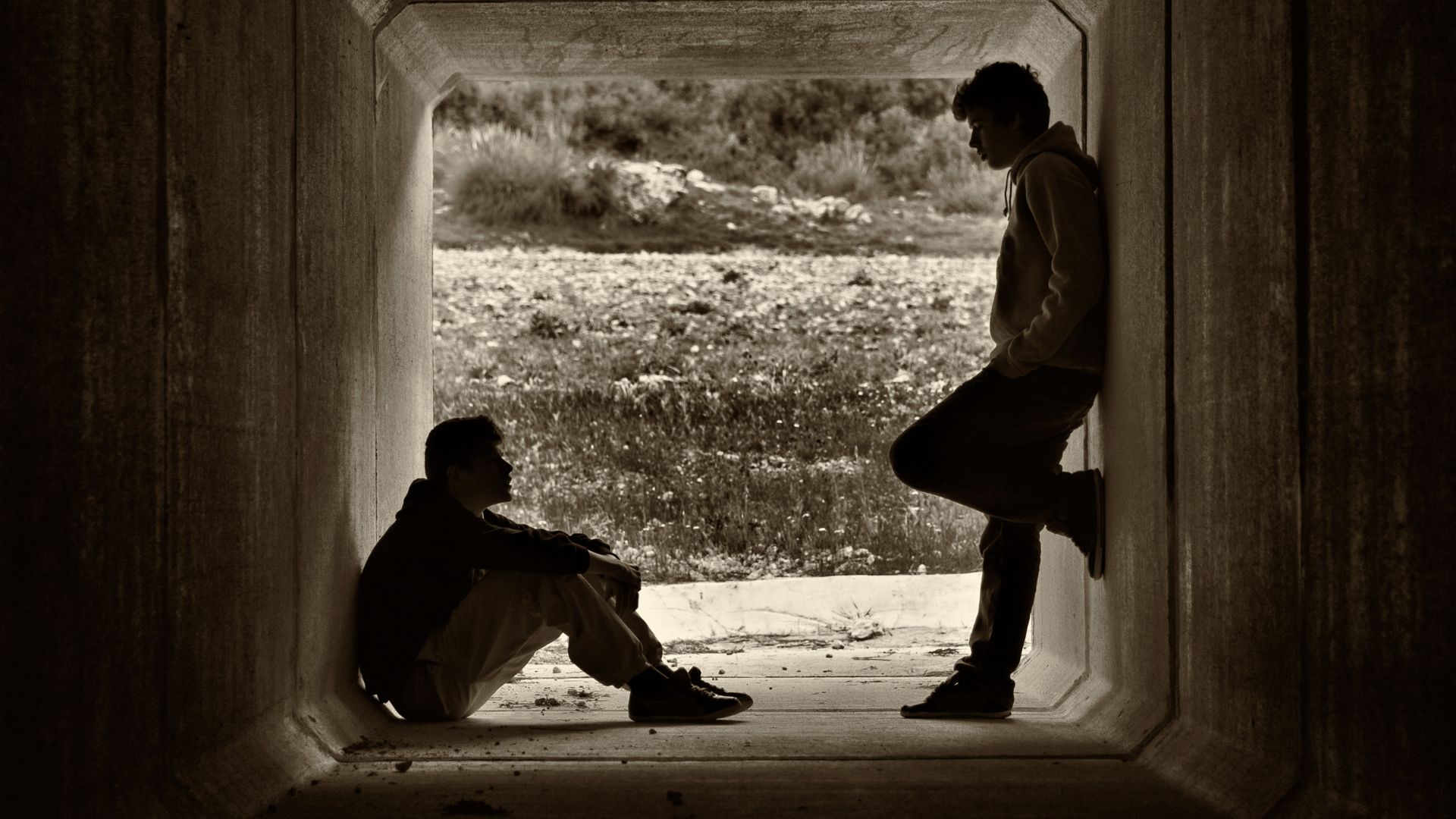 Imagem de dois homens em um túnel, um de frente para o outro, um está sentado e o outro de pé.