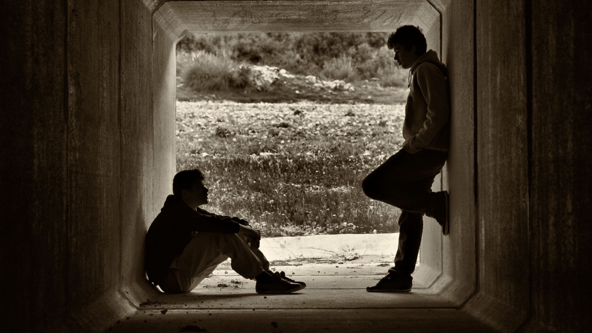 Mensagens Com Amor / Canva / Sydavia de Getty Images Signature Imagem de dois homens em um túnel, um de frente para o outro, um está sentado e o outro de pé.