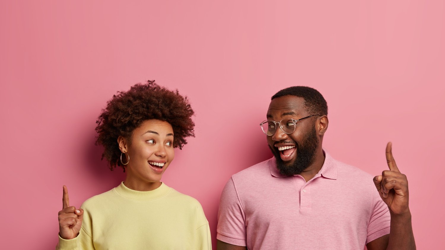 Um casal de irmãos negros apontando para cima enquanto ambos sorriem.