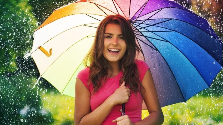 Garota sorrindo com guarda-chuva aberto enquanto chove