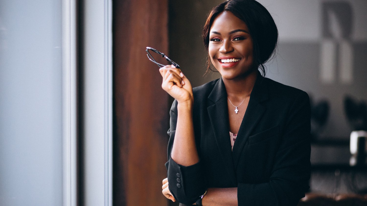 senivpetro / Freepik Mulher negra de terno segurando seu óculos e sorrindo