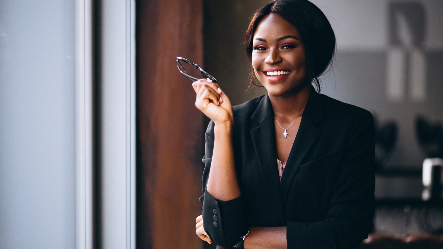 Mulher negra de terno segurando seu óculos e sorrindo