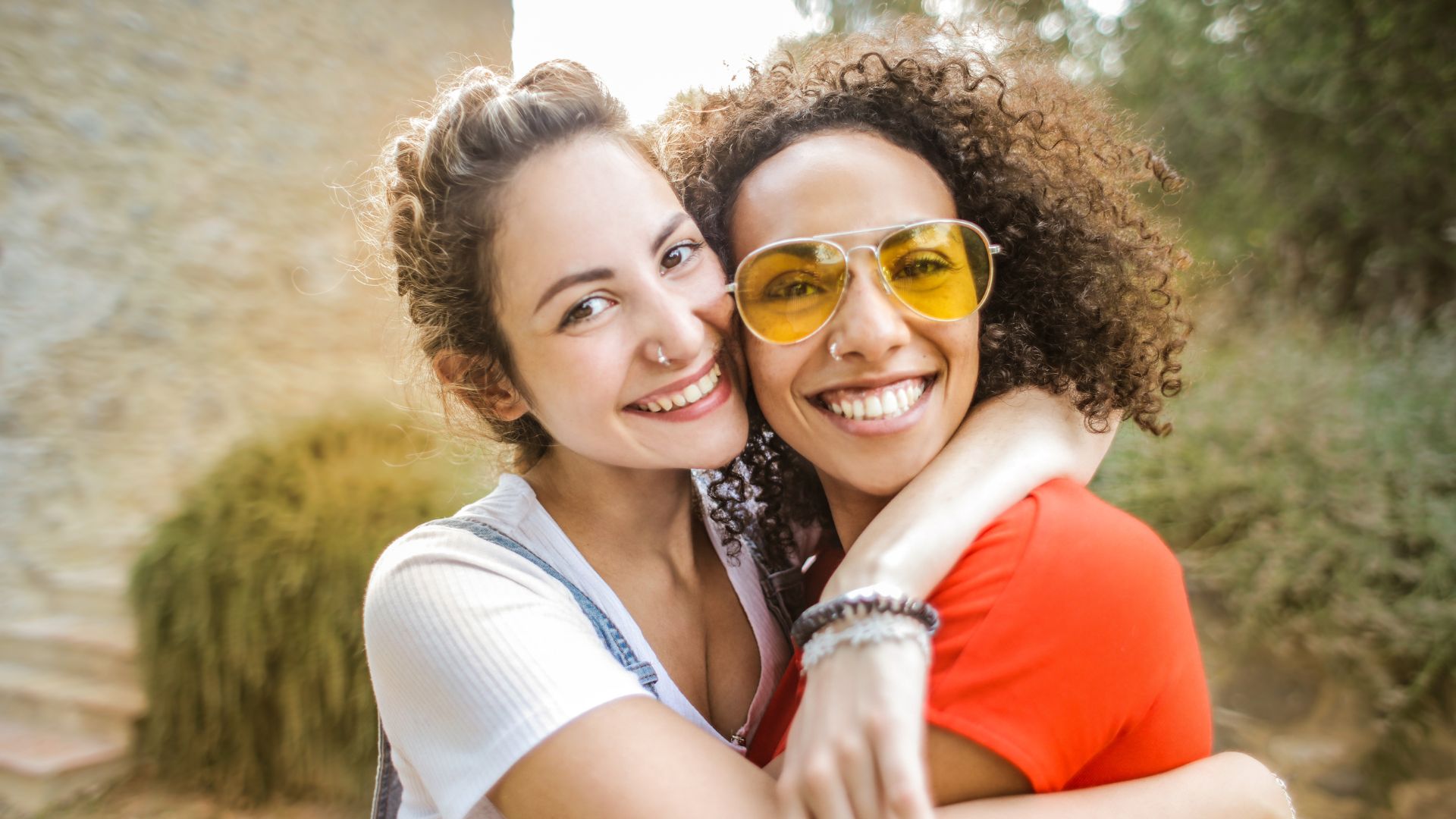 Imagem de duas mulheres abraçadas, de rosto colado e sorrindo