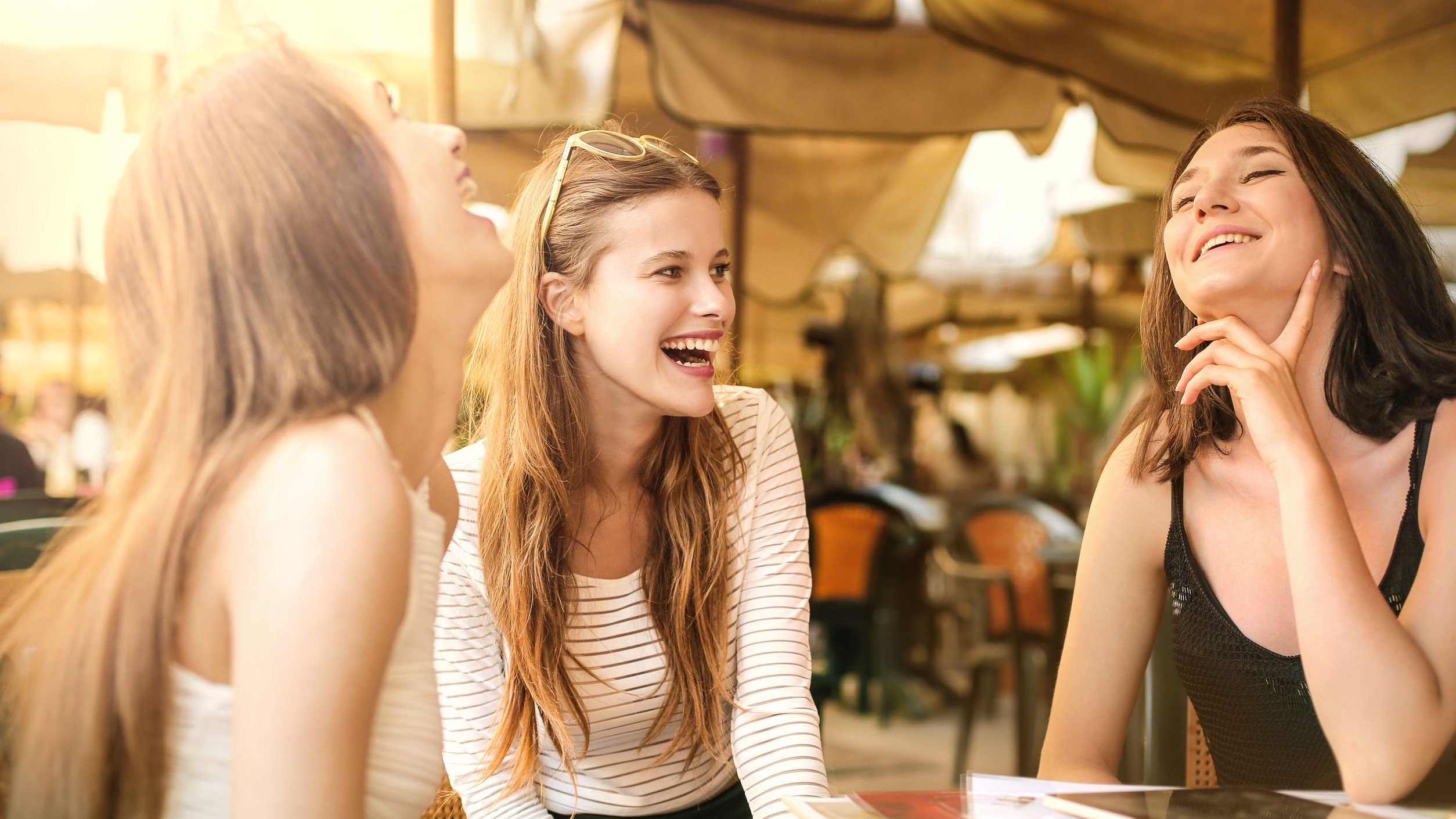 Mulheres brancas sorrindo na área externa de um restaurante.