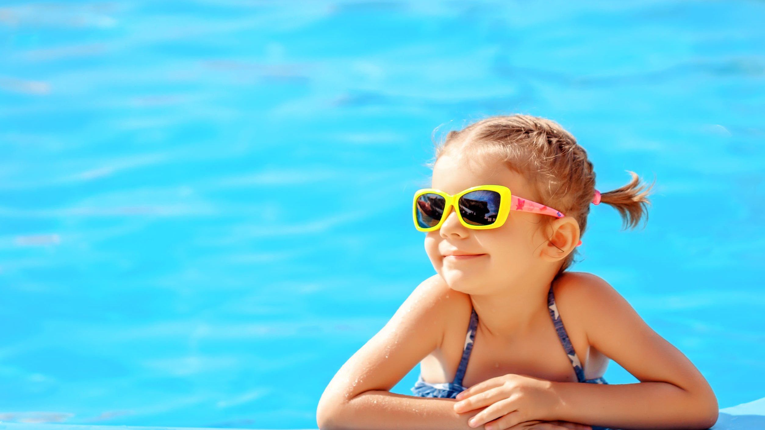 Criança apoiada na beira da piscina sorrindo