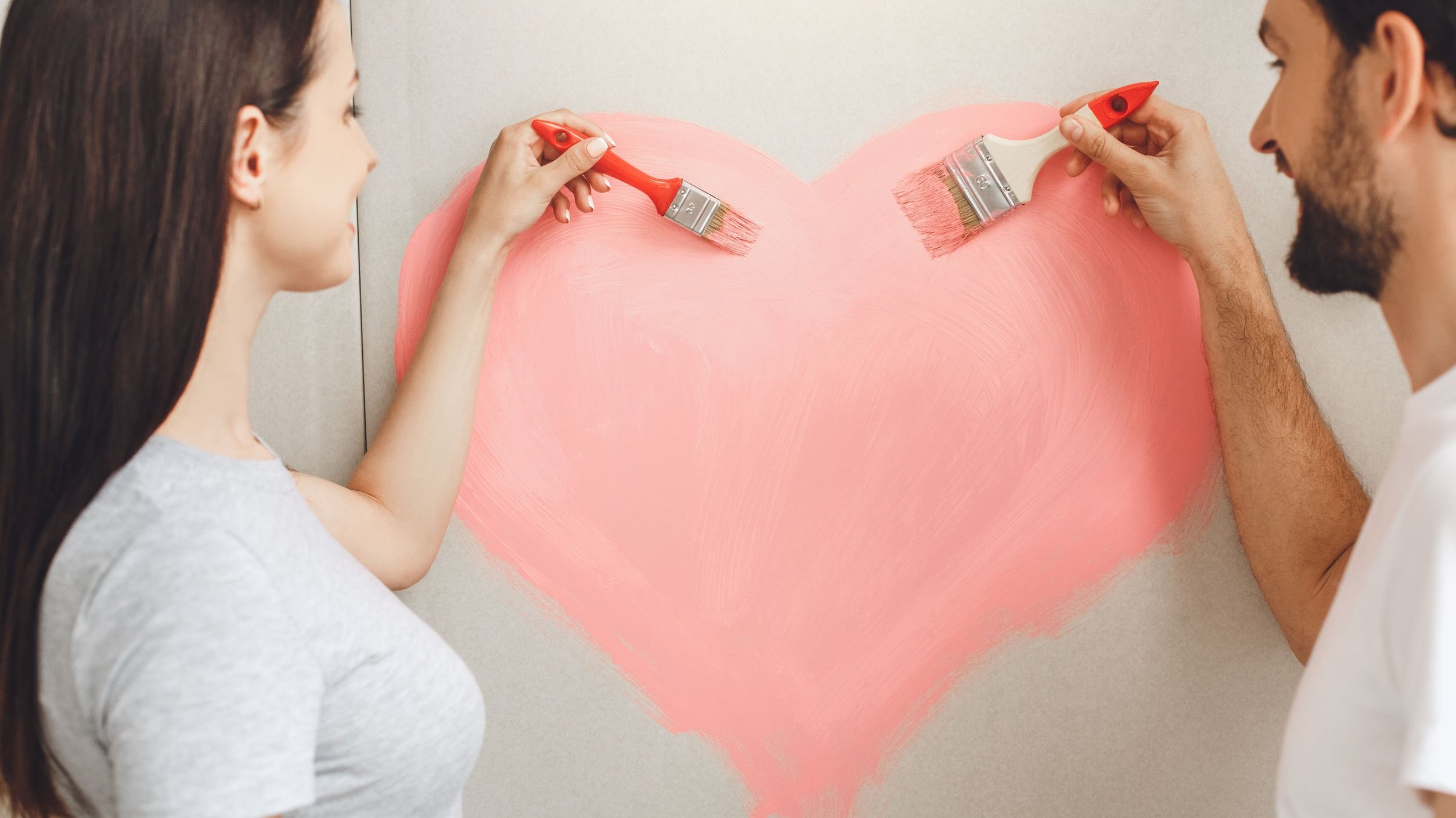 Casal pintando um coração na parede.