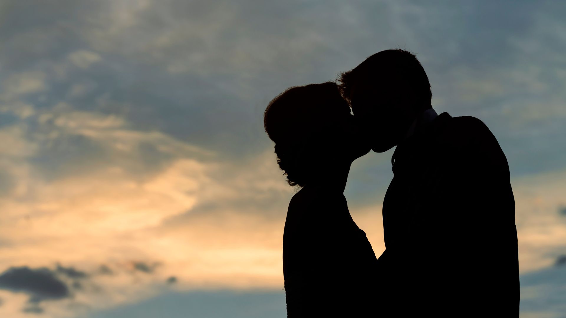 Imagem de um casal se beijando e de fundo um céu azul e alaranjado
