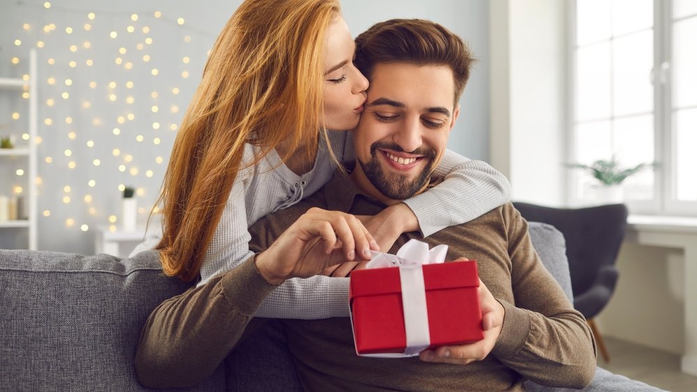 Namorada entregando um presente para seu companheiro, enquanto o beija.