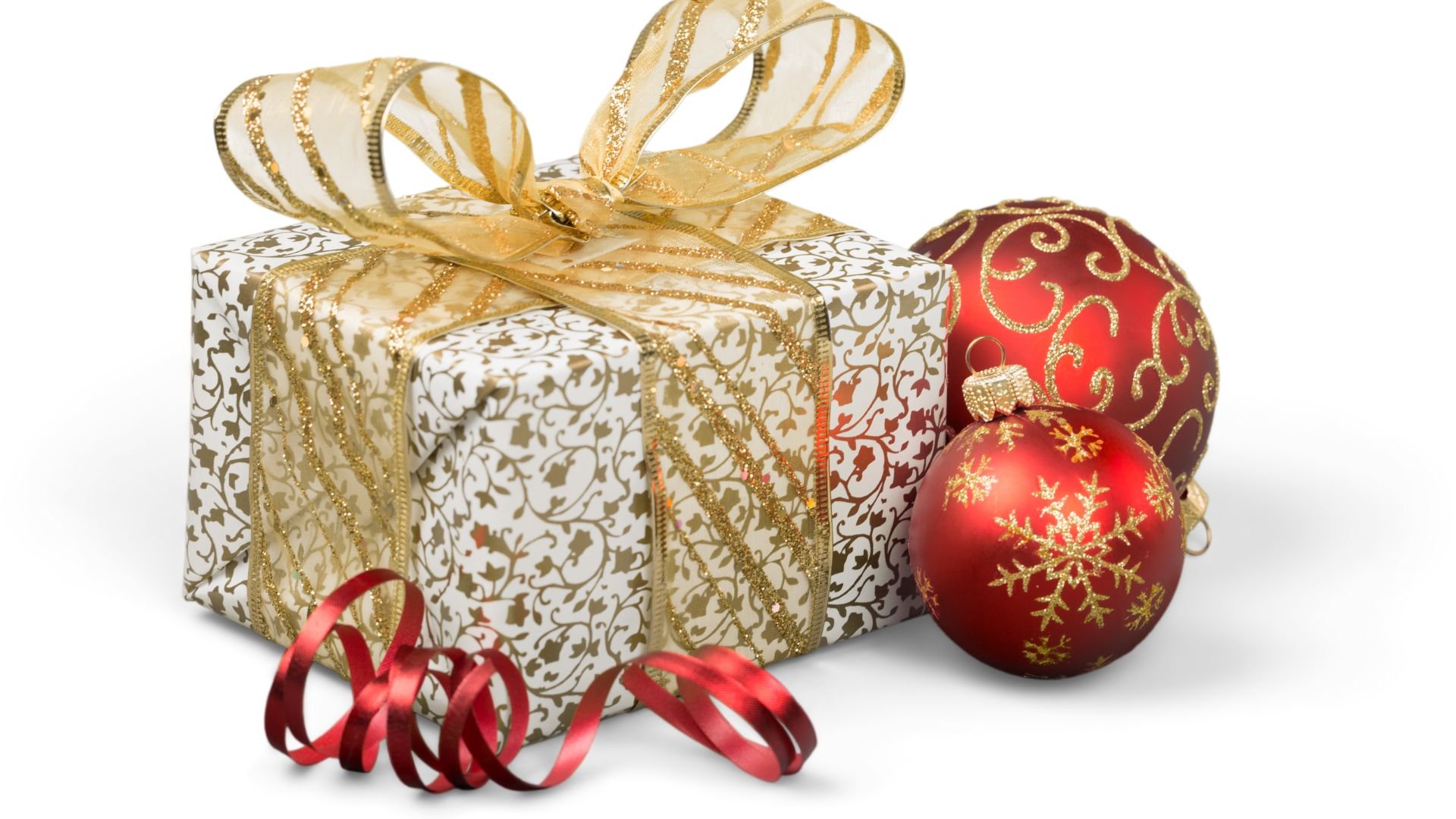 Imagem de fundo branco. Em destaque temos uma caixa de presente embrulhada em um papel branco decorada com desenhos dourados. Um laço de fita dourado está envolto da caixa e ao lado duas bolas de Natal nas cores vermelho e dourado.