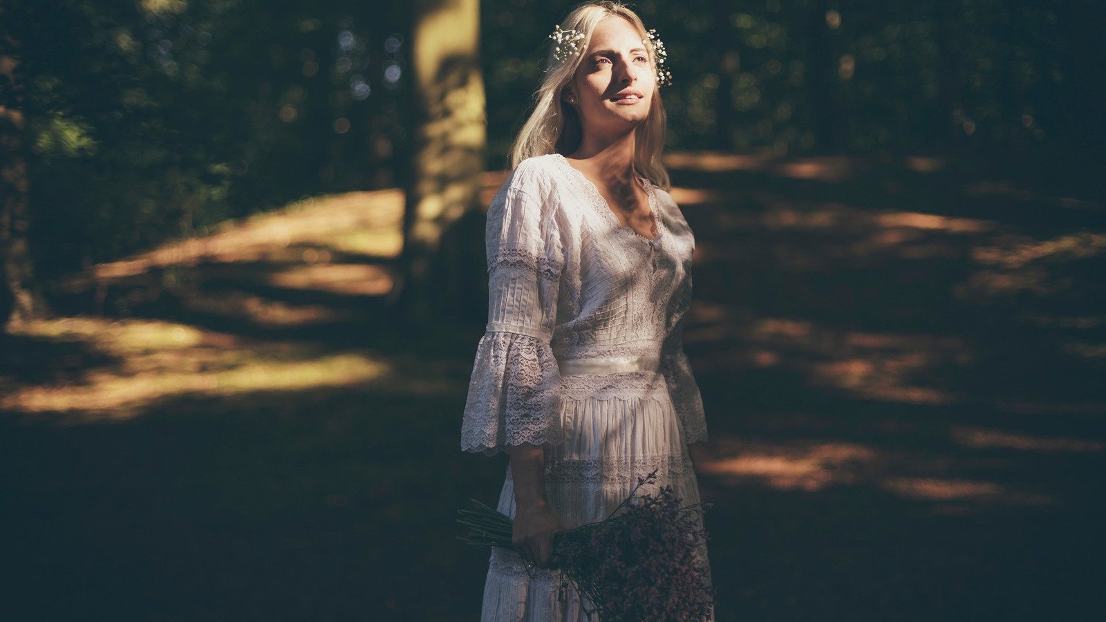 ysbrandcosijnfotografie / Canva PRO Mulher branca e loira numa floresta, com luz do sol no rosto.