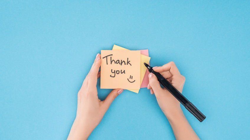 Pessoa com caneta preta escrevendo Thank You em post-it