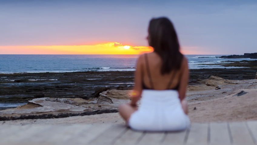 Menina sentada na praia apreciando o pôr do sol