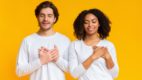 Duas pessoas de olhos fechados e com as duas mãos posicionadas no coração