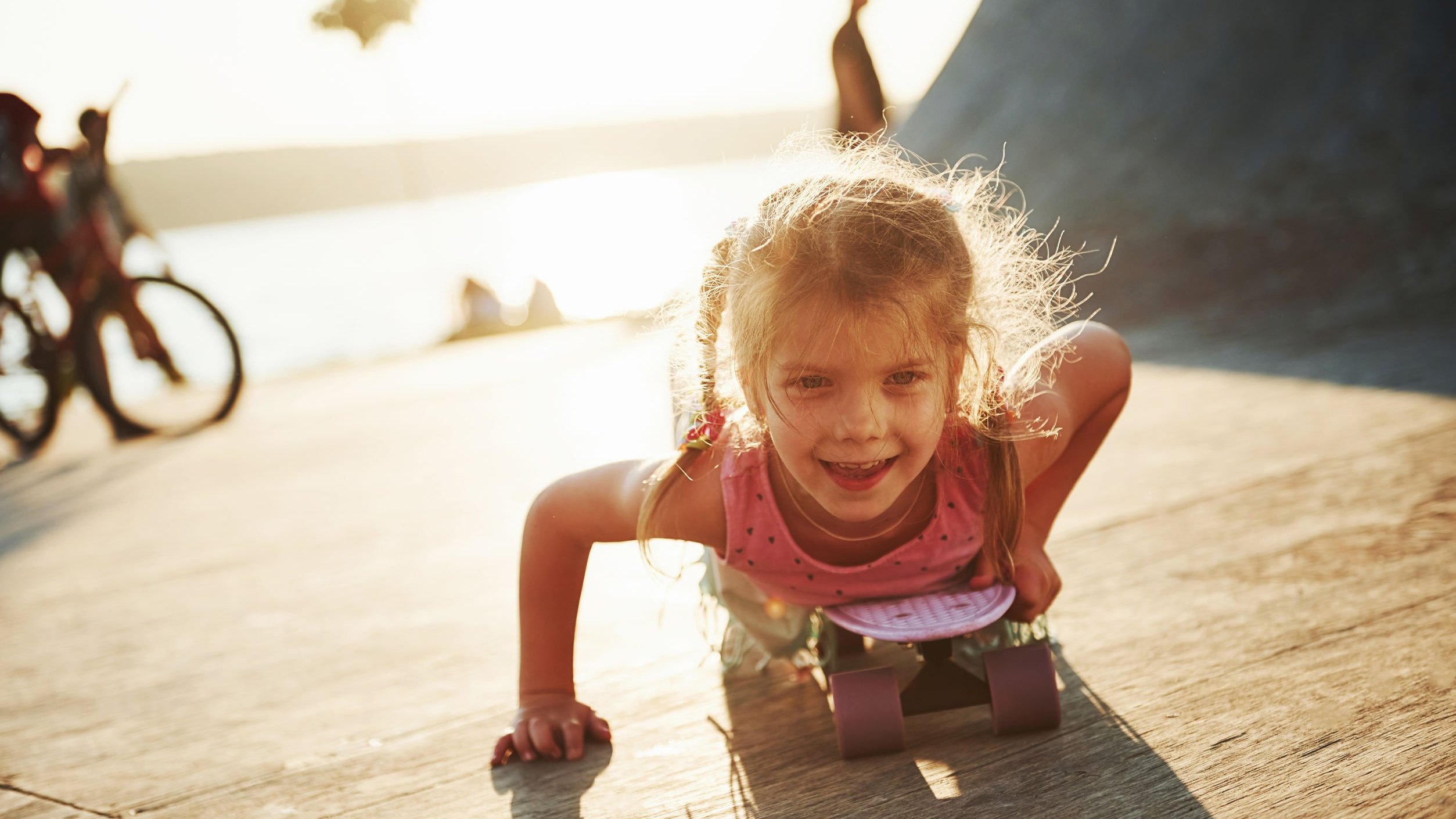 Menina deitada de bruços sobre um skate.