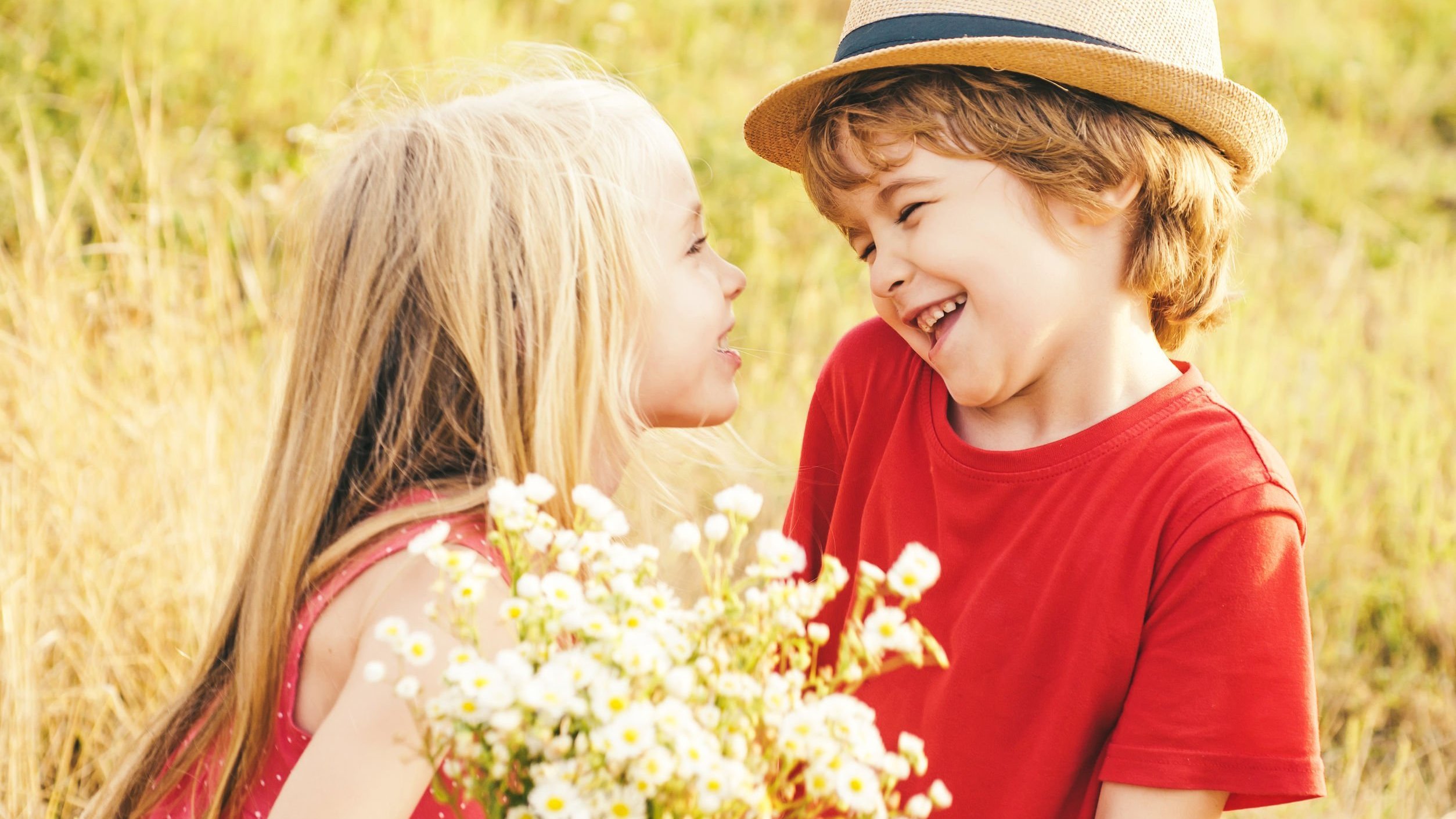 Menina e menino brancos segurando flores com expressões felizes.