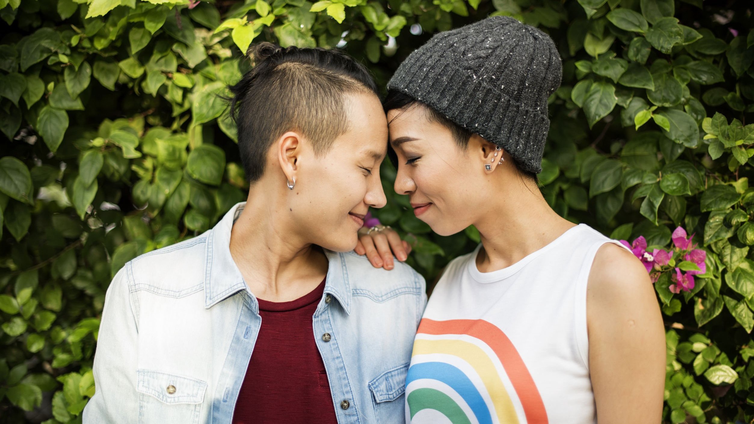 Duas mulheres uma de frente para a outra de olhos fechados e sorrindo