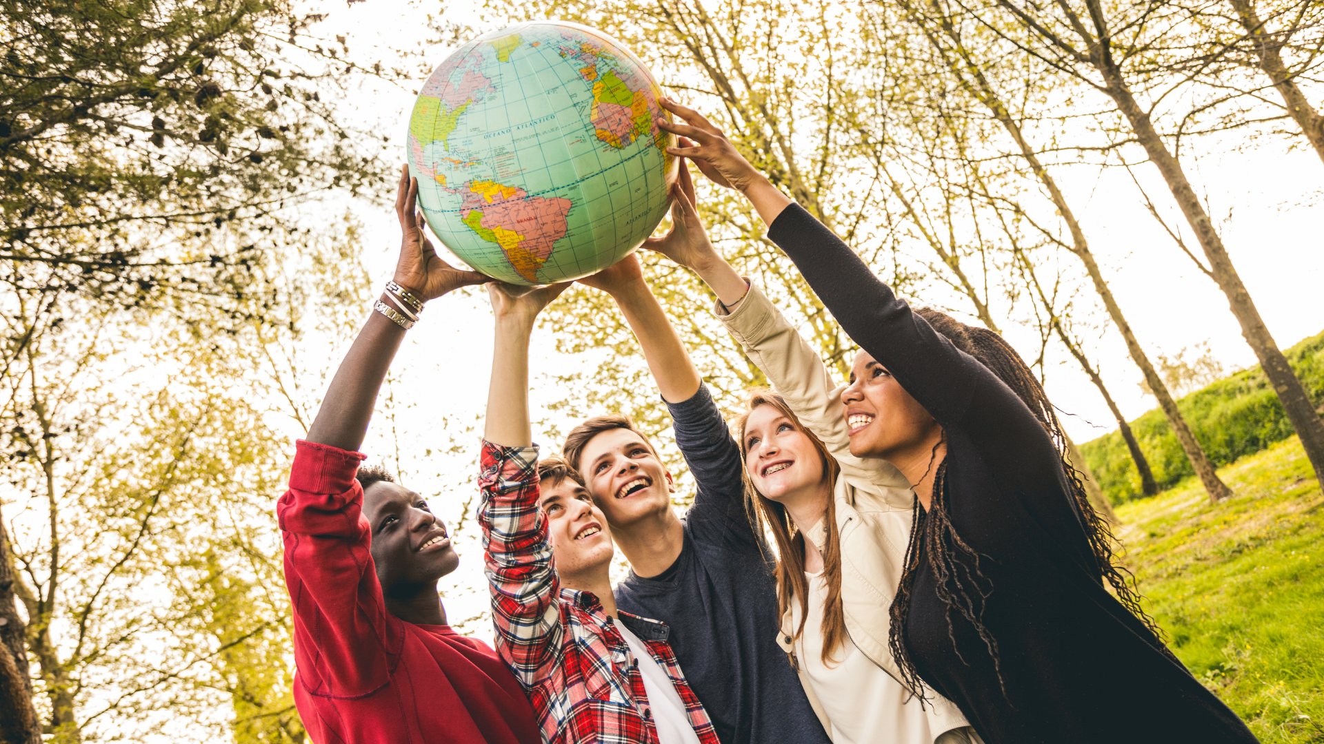 Grupo de jovens sorrindo e erguendo um globo terrestre para cima