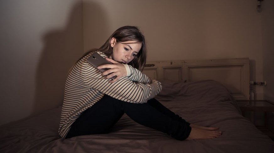 123rf / Sam Wordley Menina sentada em cama com expressão abatida