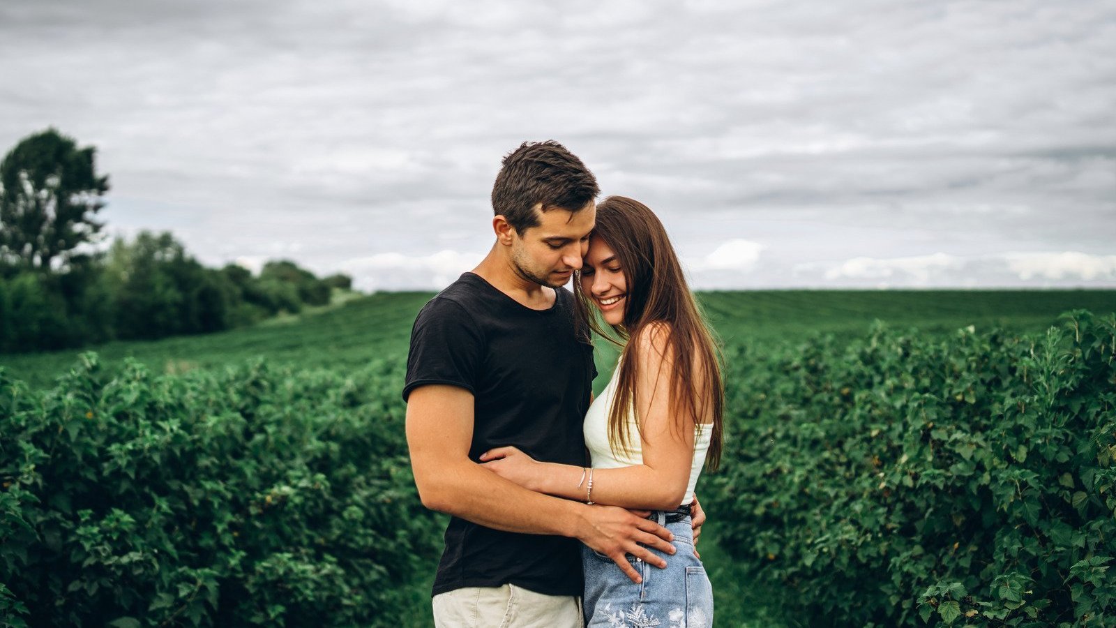 Homem e mulher brancos, abraçados num campo.