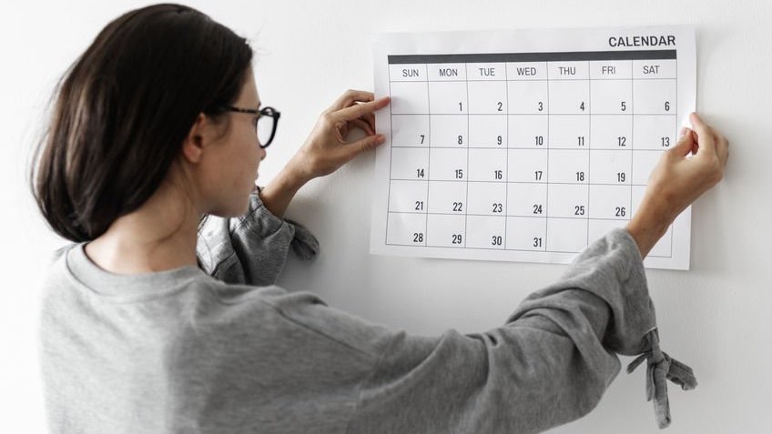 123rf / rawpixel Mulher colocando calendário na parede