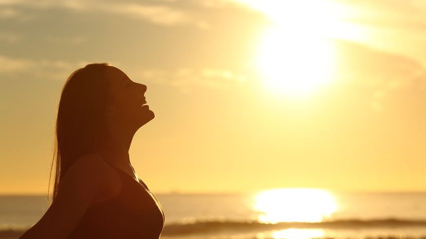 Vista lateral de mulher respirando ar fresco ao amanhecer na frente do sol