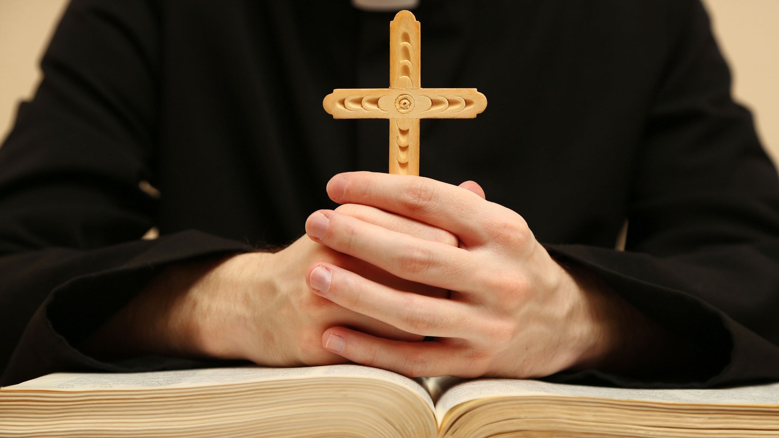Mãos unidas segurando cruz de madeira sobre bíblia