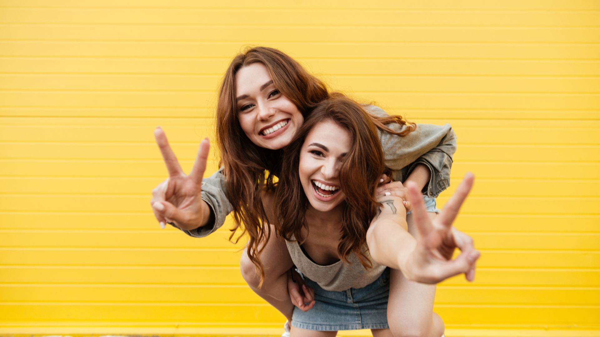 Imagem de fundo amarelo e em destaque duas amigas felizes e se divertindo no dia do aniversário de uma delas.