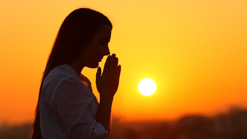 Mulher orando com o pôr do sol ao fundo