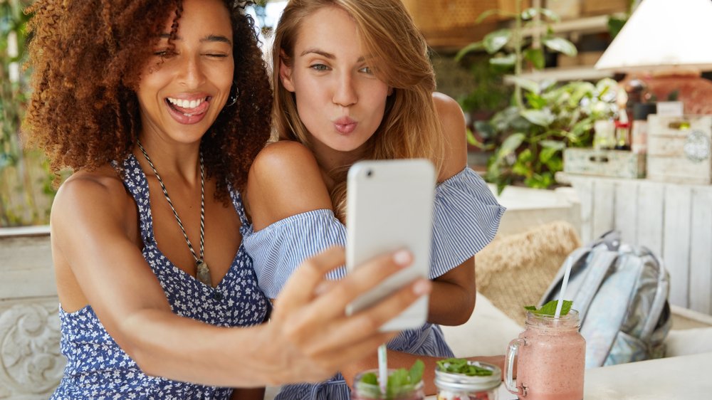 Amigas jovens interraciais tirando selfie com caretas
