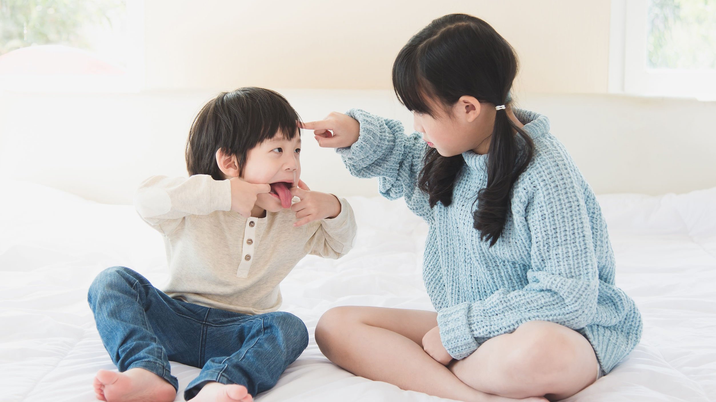 Irmão e irmã asiáticos brincando numa cama branca