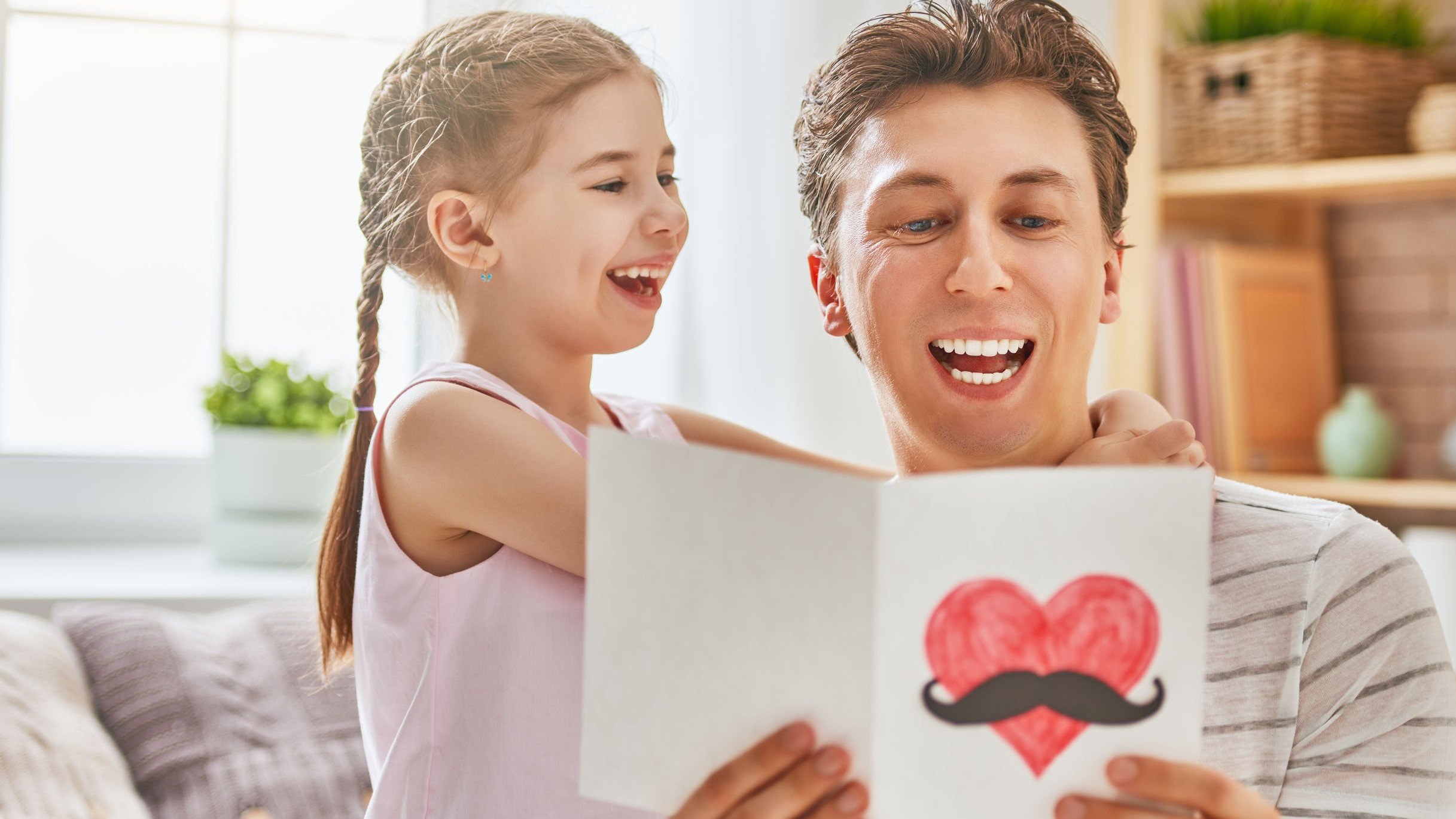 Pai lendo cartão de dia dos pais com a filha ao lado, abraçando-o