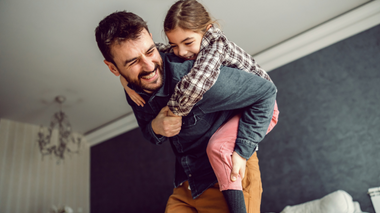 Pai e filha brincando de cavalinho e sorrindo.