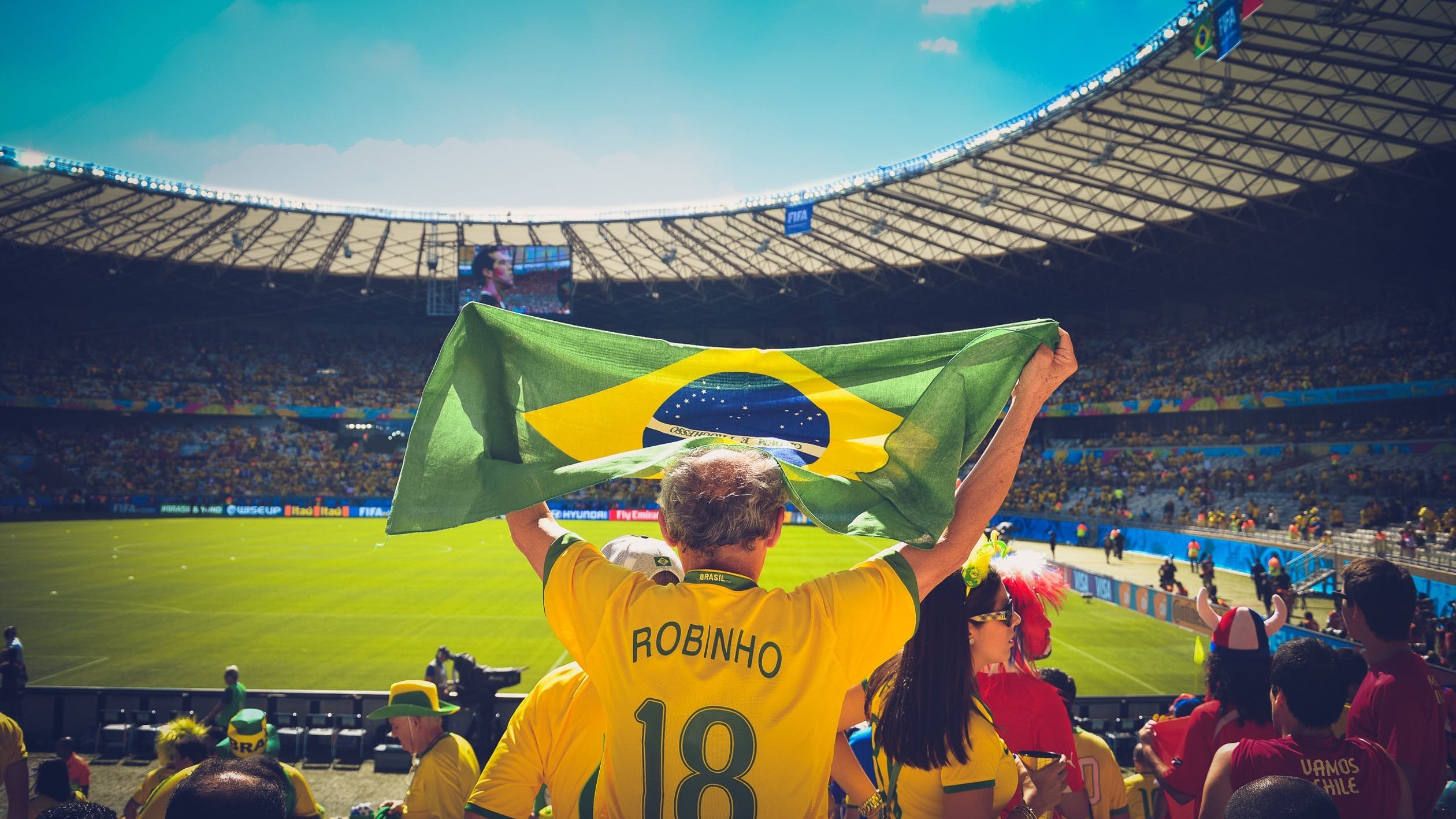 Homem segurando bandeira do Brasil em estádio