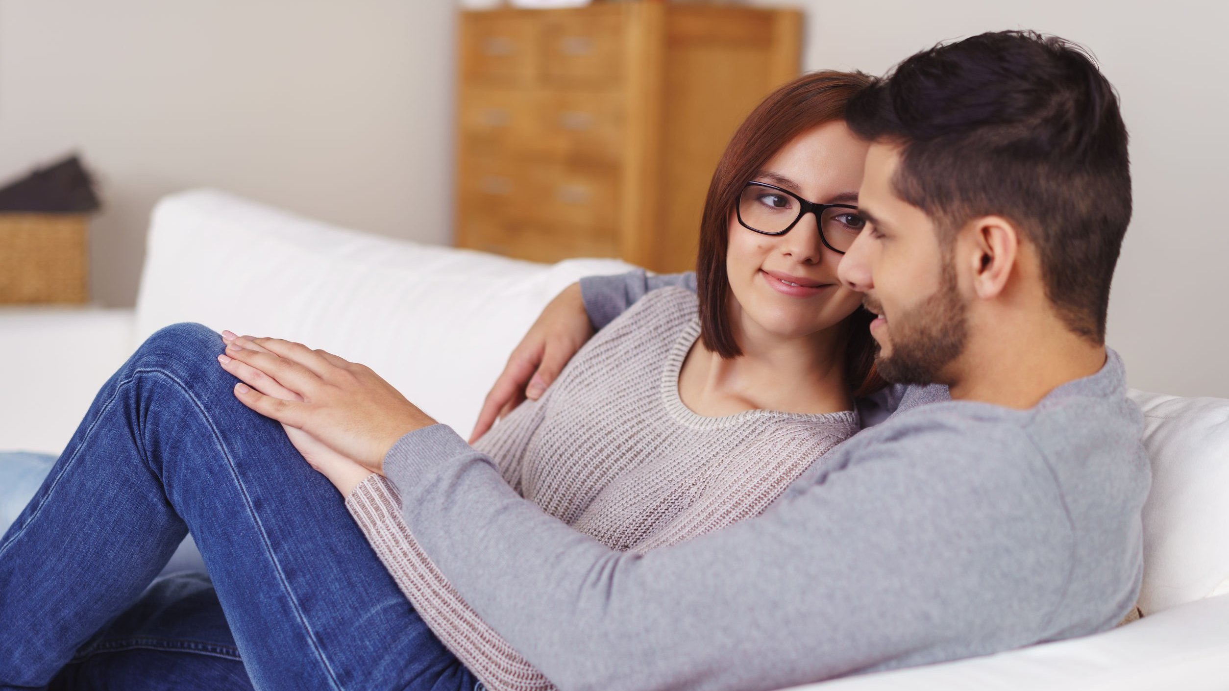 Casal deitado no sofá com as mãos entrelaçadas.