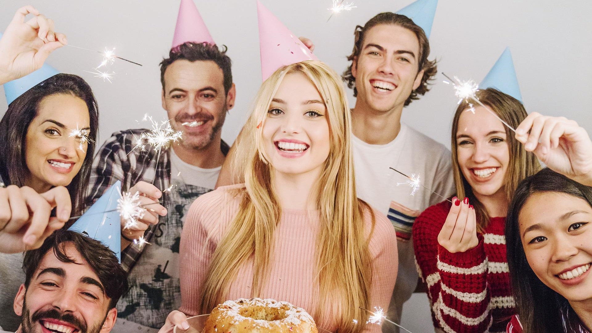 Seis pessoas estão comemorando um aniversário com velas, chapéus coloridos e um bolo