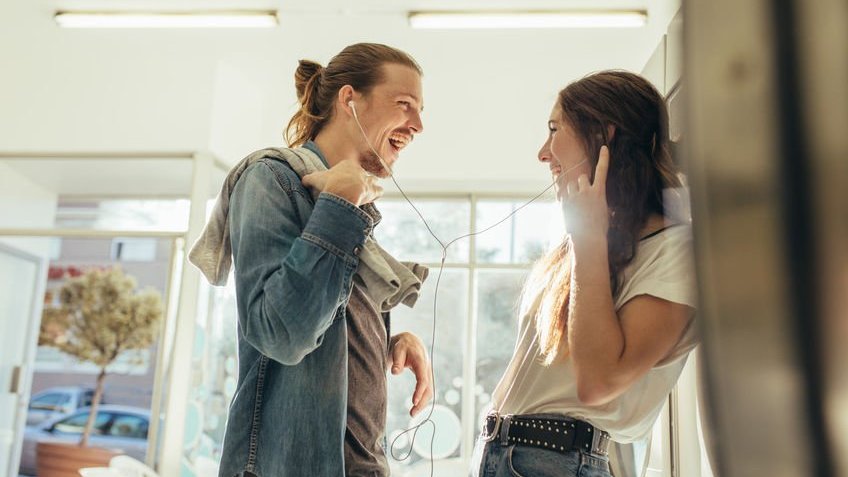 Casal em pé na cozinha dividindo fones de ouvido