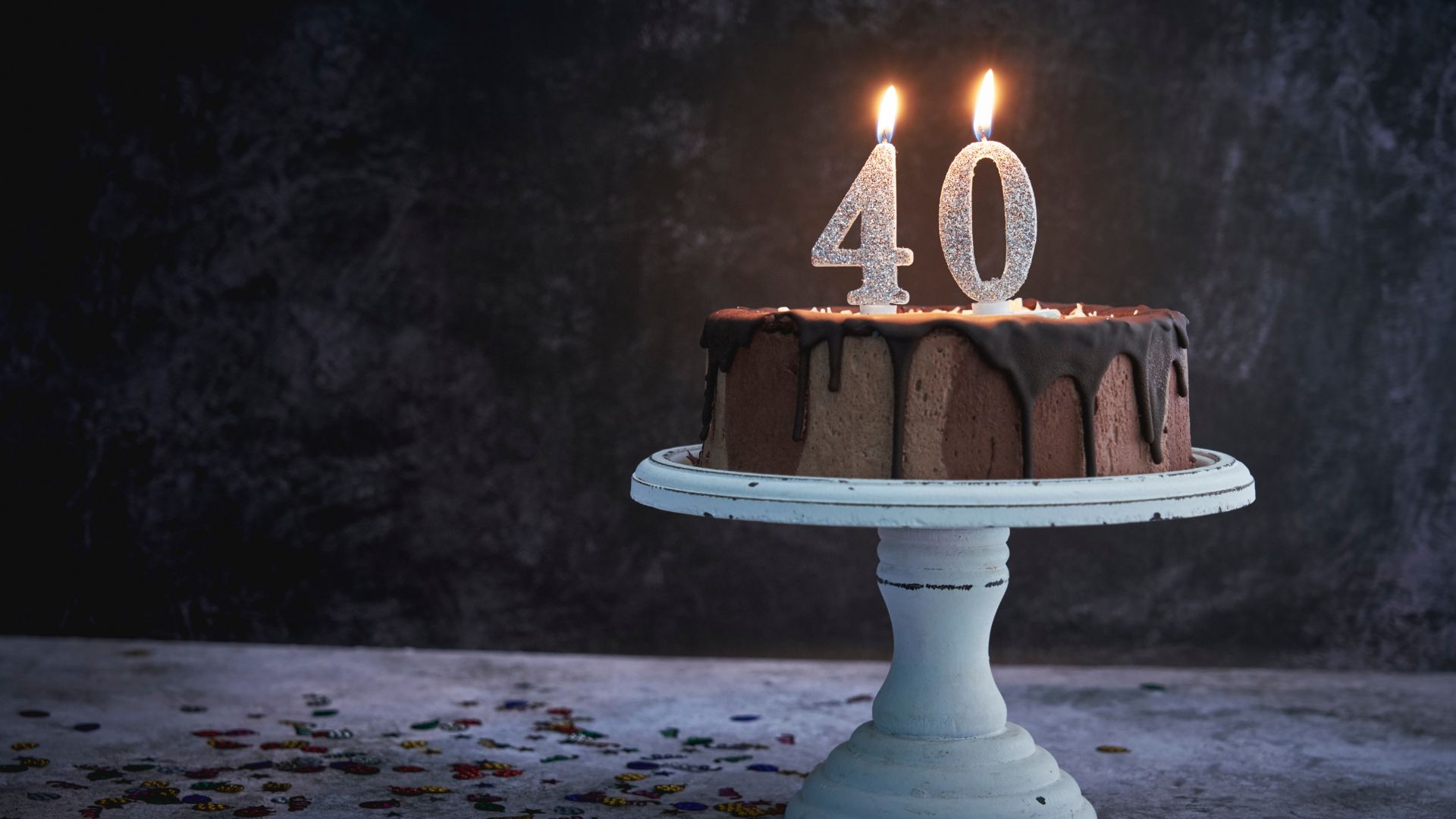 Imagem de um bolo de chocolate com velas acesas para 40 anos no topo