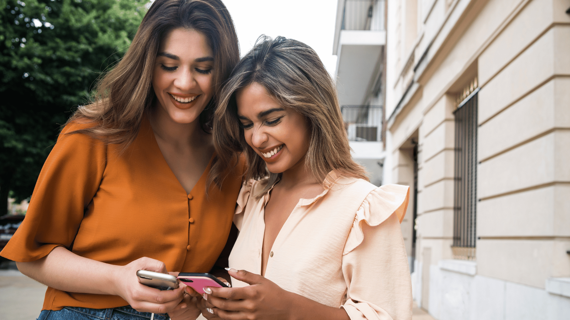 Duas amigas loiras rindo enquanto olham para os seus celulares.