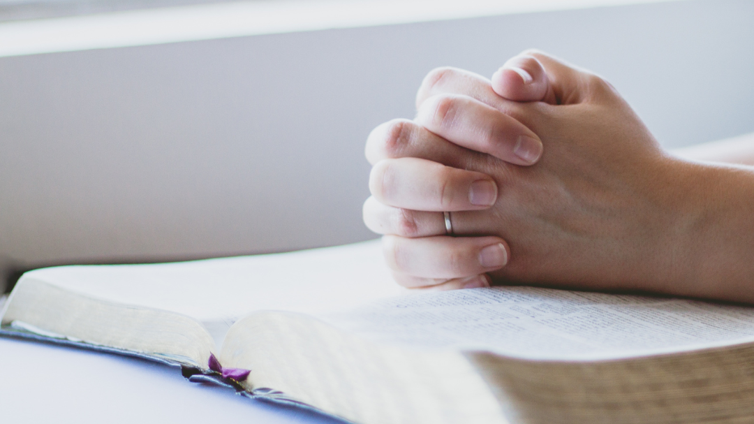 Mão feminina fechada, em sinal de oração, em cima da Bíblia.