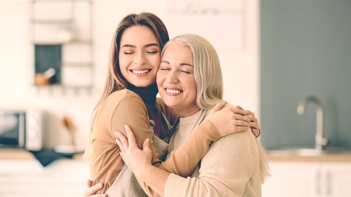 Mulher jovem e mulher de cabelos grisalhos se abraçando, ambas sorridentes.