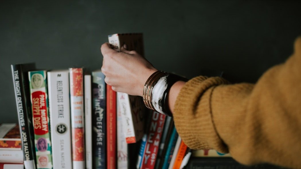 Mão pegando livro em prateleira de livros