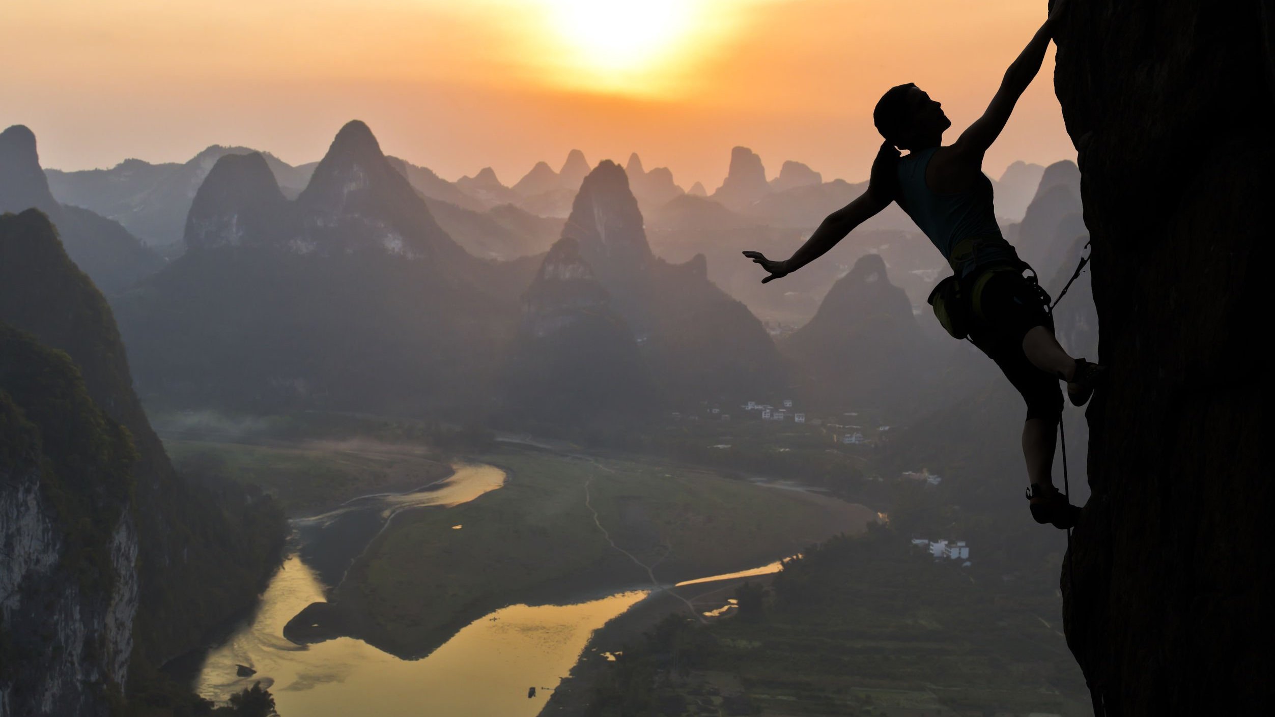 Silhueta de mulher escalando montanha no pôr-do-sol.