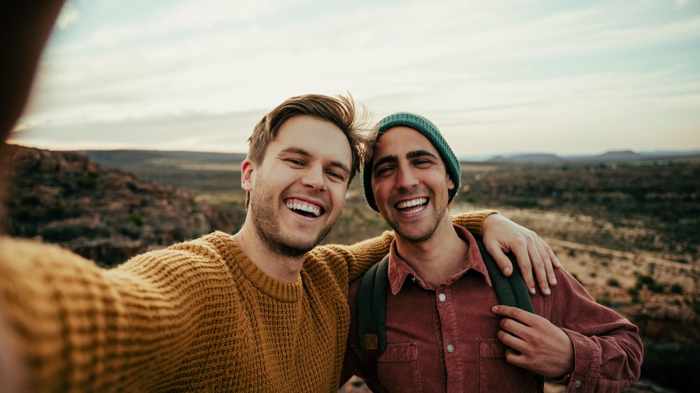 Dois amigos homens tirando selfie e sorrindo