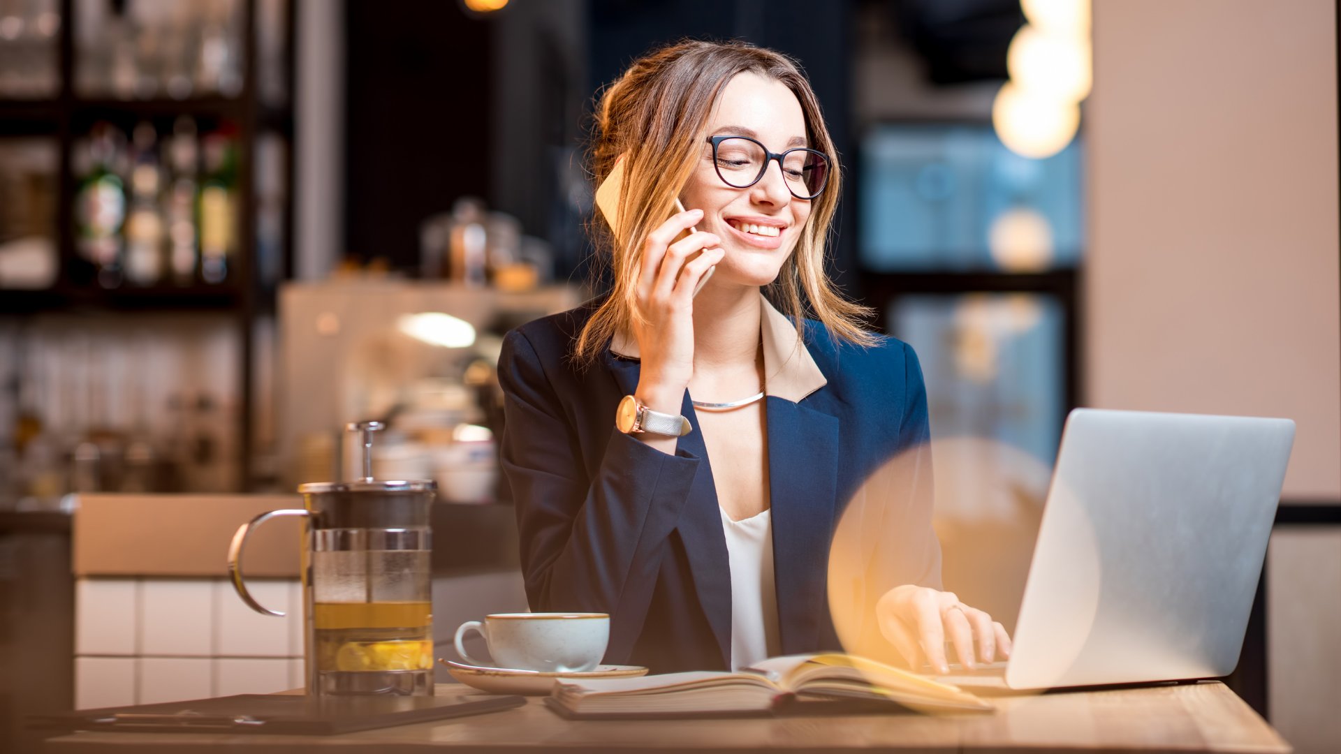 Mulher empreendedora sorrindo enquanto fala no telefone e trabalha mexendo no laptop