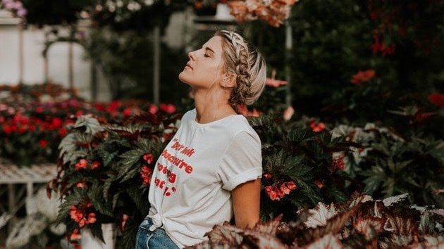 Menina de olhos fechados em meio a arbustos e flores.