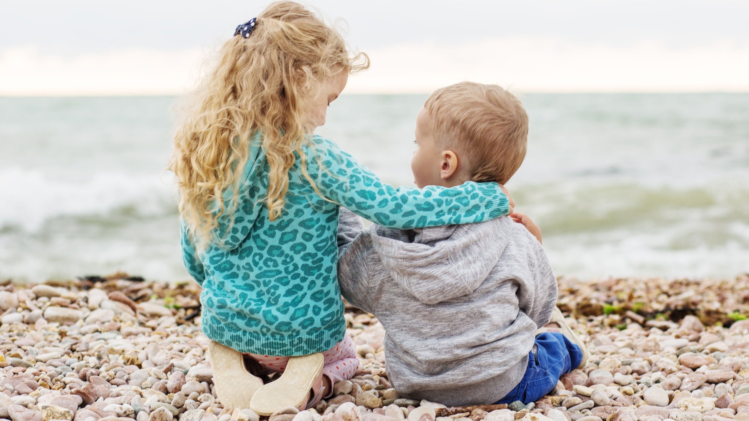 Duas crianças pequenas abraçadas em frente ao mar