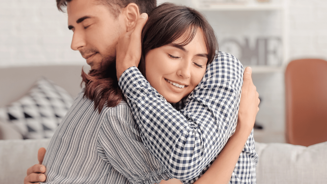 casal se abraçando, sentados no sofá.