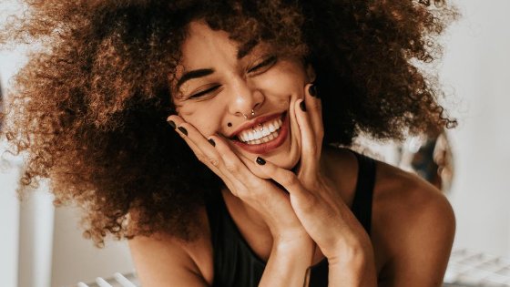 Mulher sorrindo de olhos fechados com as mãos no rosto