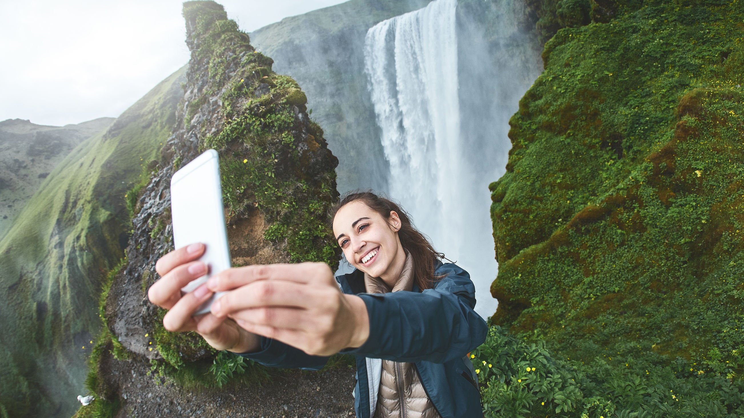 Mulher fazendo selfie com cachoeira ao fundo