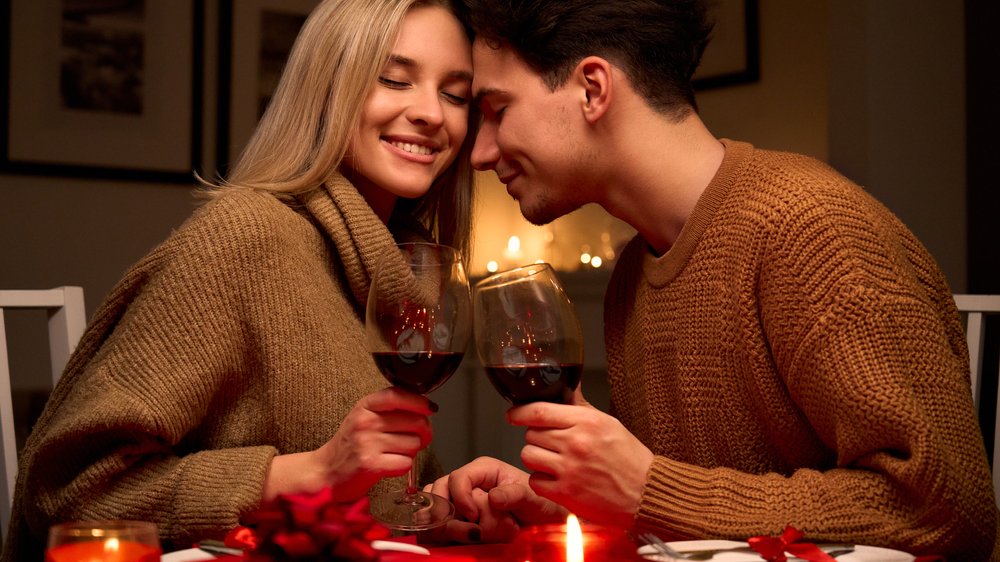Casal tomando vinho em um jantar romântico enquanto se acariciam
